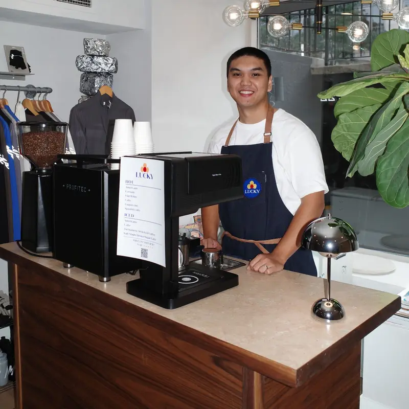 A smiling Lucky Coffee barista behind the espresso machine on the walnut coffee cart