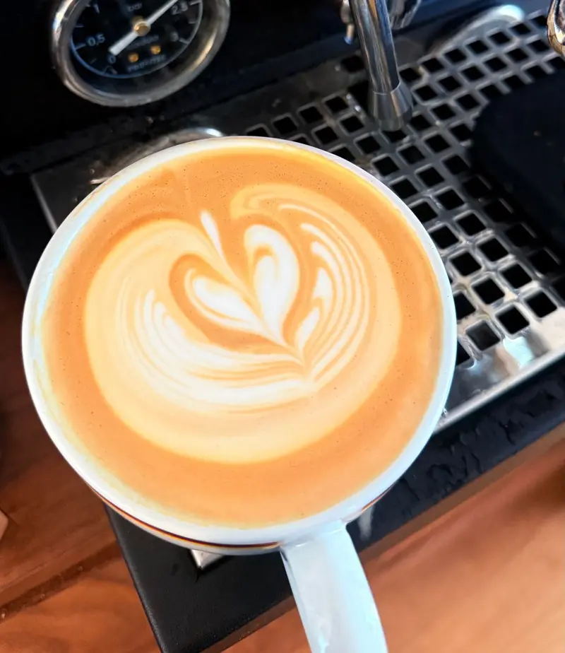 A latte with heart-shaped foam art in a white cup beside the espresso machine on the Lucky cart