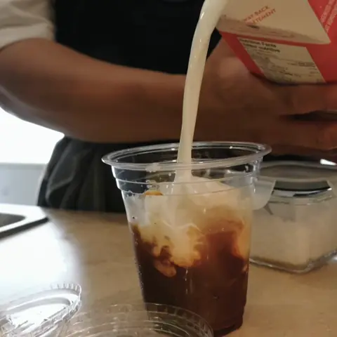 A barista pours milk into an iced coffee on the Lucky cart